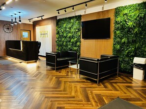 Un espace d’accueil doté d’un comptoir de réception en bois, de canapés en cuir noir, d’un grand téléviseur fixé au mur et d’un jardin vertical verdoyant.