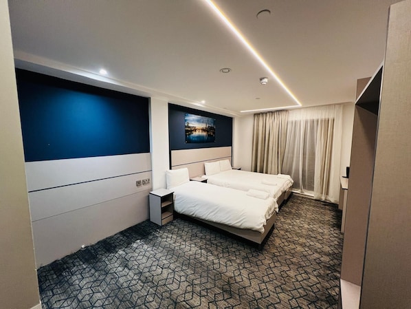 Une chambre d’hôtel avec deux lits, une grande fenêtre avec des rideaux, un tableau au mur et une moquette à motifs.