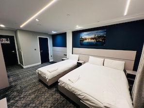 Une chambre d’hôtel avec deux lits, une table de chevet, un bureau et une grande fenêtre donnant sur le paysage urbain.
