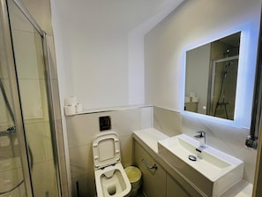 Une salle de bain moderne avec une douche à parois de verre, des toilettes et un lavabo surmonté d’un miroir.