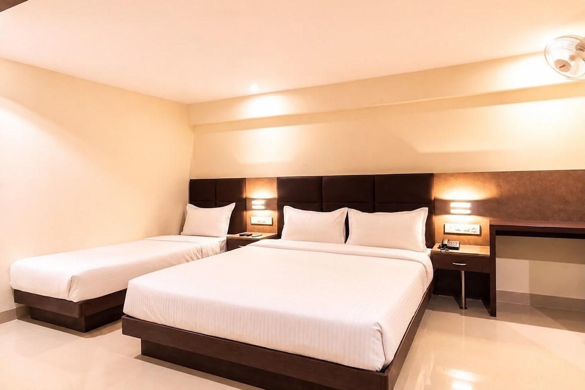 Habitación de hotel con dos camas, un cabecero oscuro, lámparas de noche y un televisor de pantalla plana.
