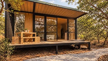 A modern wooden structure with large glass windows, a wooden deck, and a gravel path.