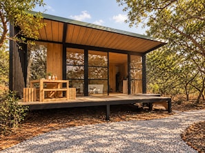 A modern wooden structure with large glass windows, a wooden deck, and a gravel path.
