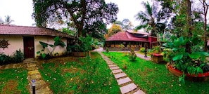 A garden pathway leading to a building with a red roof, surrounded by lush greenery and palm trees. - Ira Marari (Mararikkulam North)