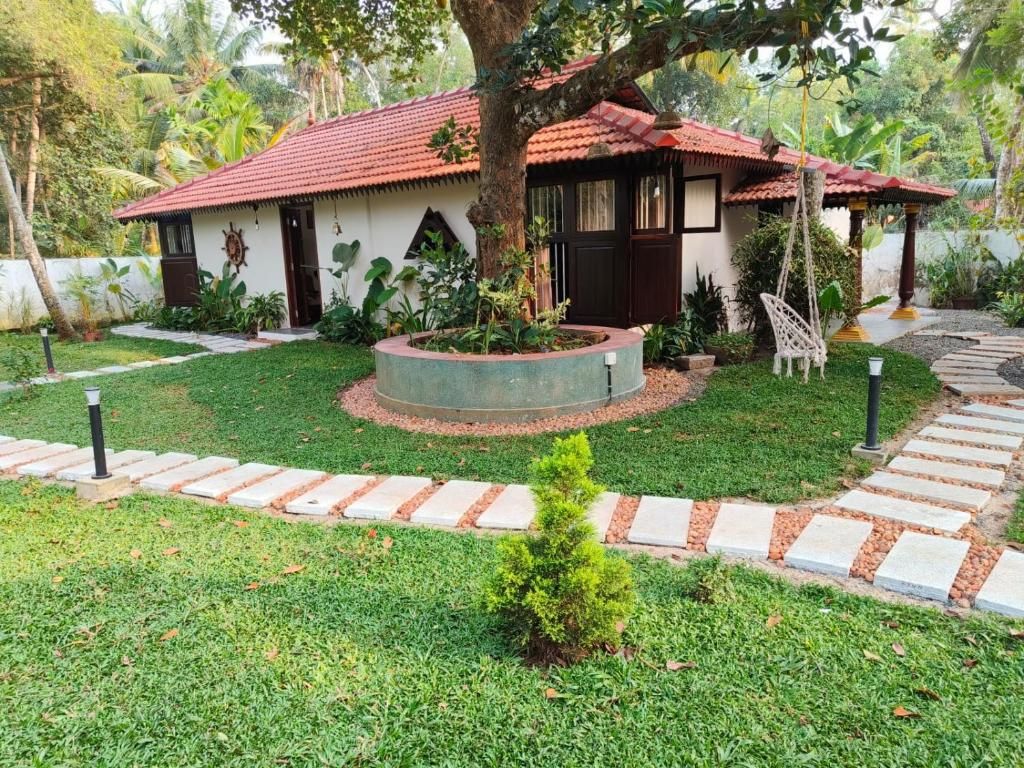 Una casa con techo de tejas rojas, rodeada por un jardín bien cuidado con un vivero circular y un pequeño árbol.