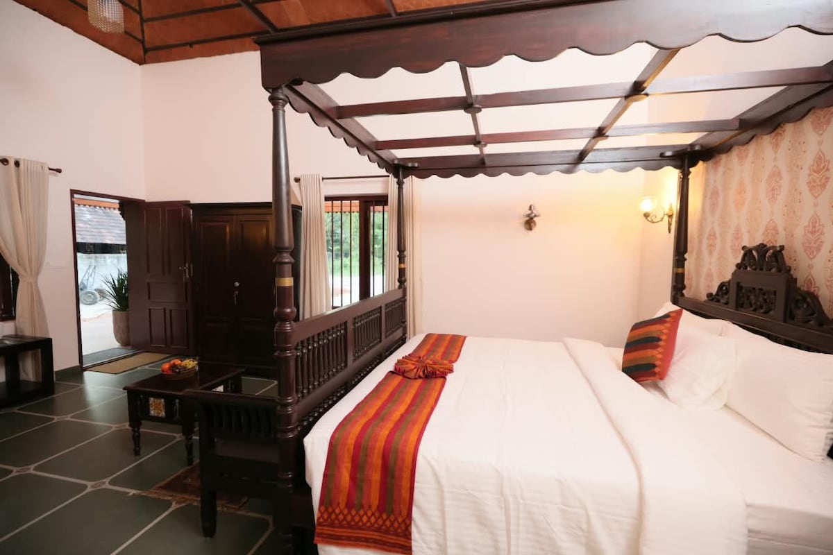 Une chambre traditionnelle avec un lit à baldaquin, un bureau en bois et une vue sur l’extérieur par une fenêtre.