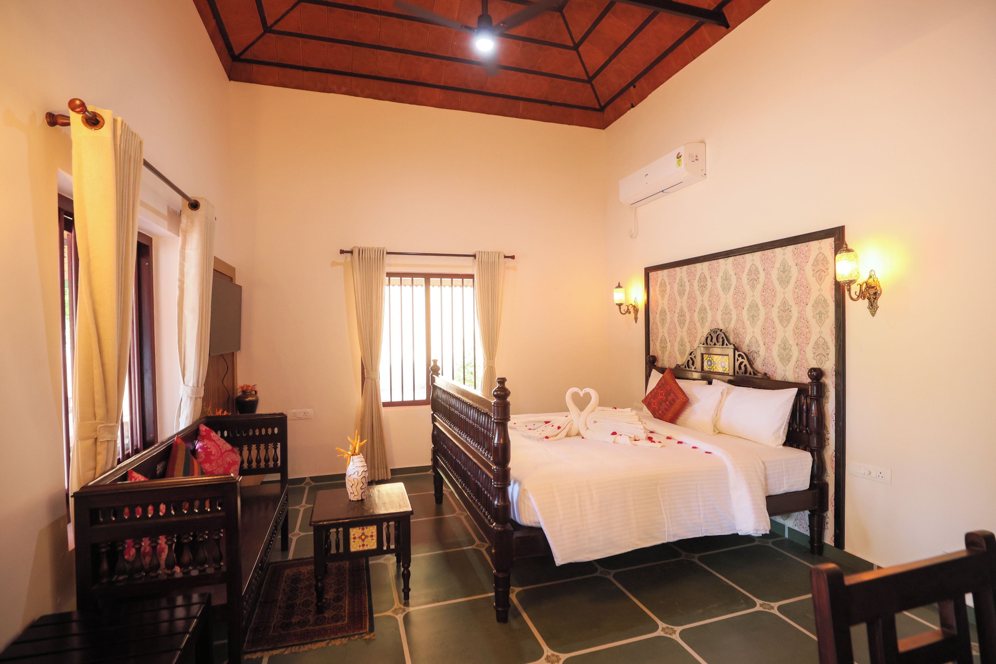 A hotel room with a bed, a desk, a chair, a window with curtains, and a ceiling fan.