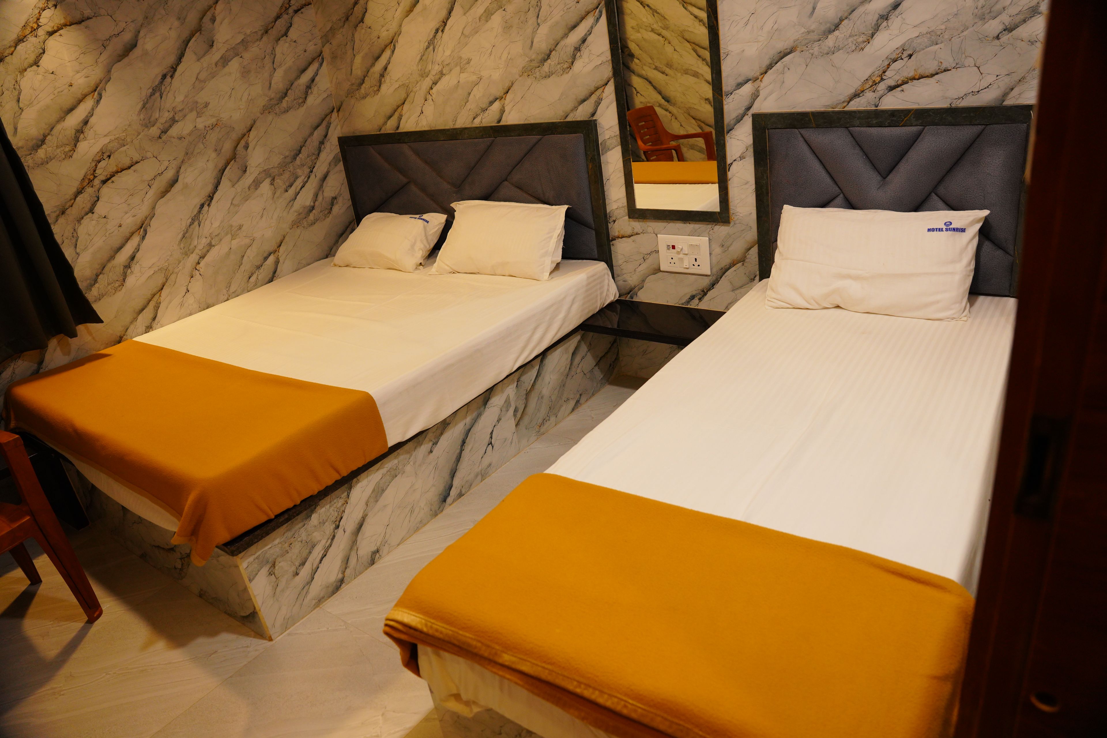 A hotel room with two beds, marble walls, and a nightstand with a lamp.