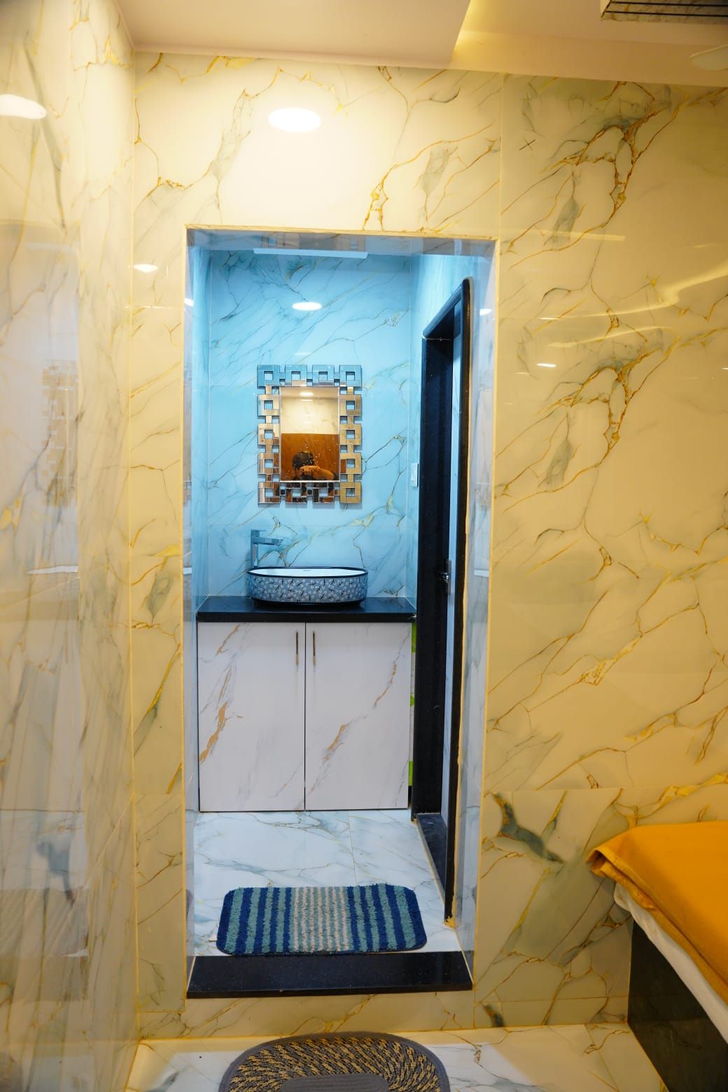 Un baño con pared de mármol, un lavabo con espejo decorativo y un perchero para toallas.