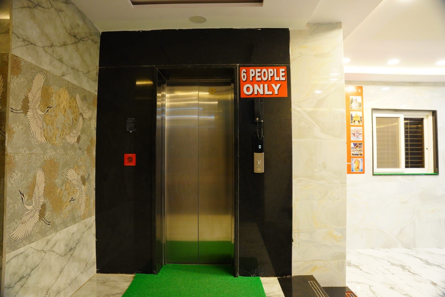 An elevator with a '6 PEOPLE ONLY' sign, marble walls, and a green carpeted floor.