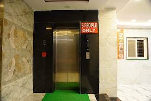 Un ascensor con un cartel que dice 'SOLO 6 PERSONAS', paredes de mármol y piso cubierto de alfombra verde.
