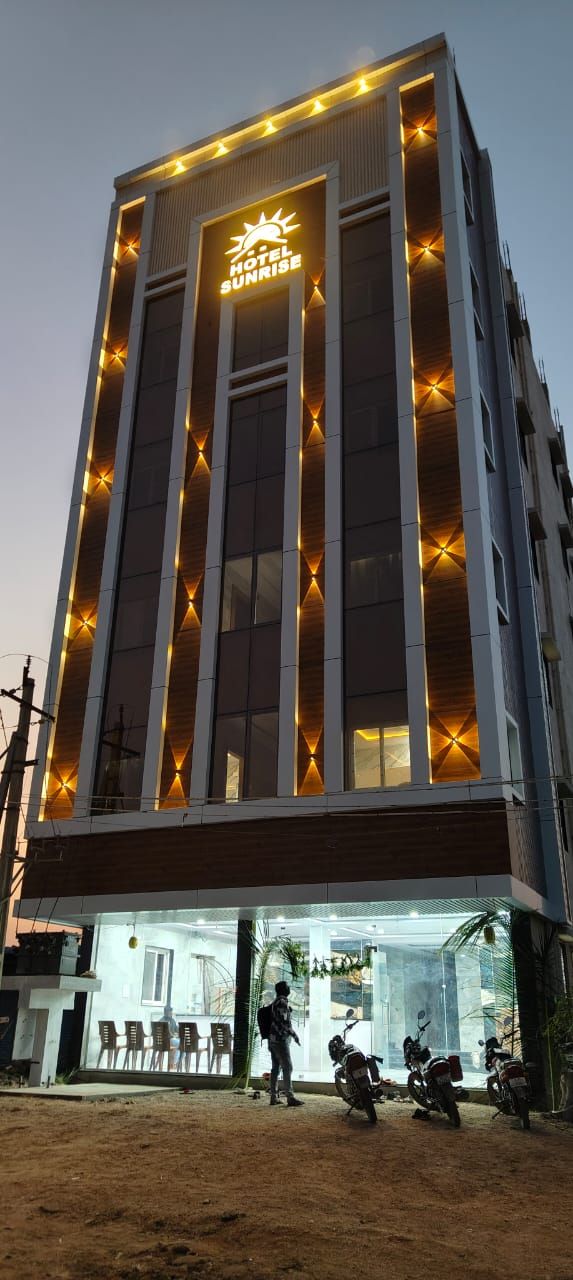 Un edificio de hotel con un letrero que dice 'HOTEL SUNRISE' y una entrada a nivel de calle con área de descanso y motocicletas estacionadas afuera.