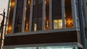 Un edificio de hotel con un letrero que dice 'HOTEL SUNRISE' y una entrada a nivel de calle con área de descanso y motocicletas estacionadas afuera.