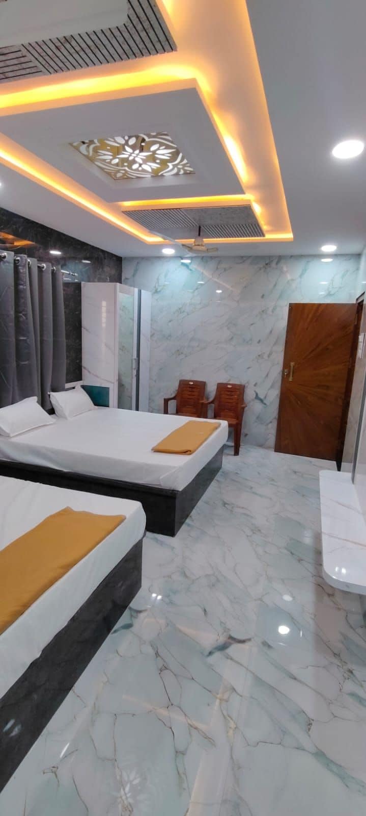 A hotel room with two beds, marble flooring, a wooden door, and a ceiling with recessed lighting.