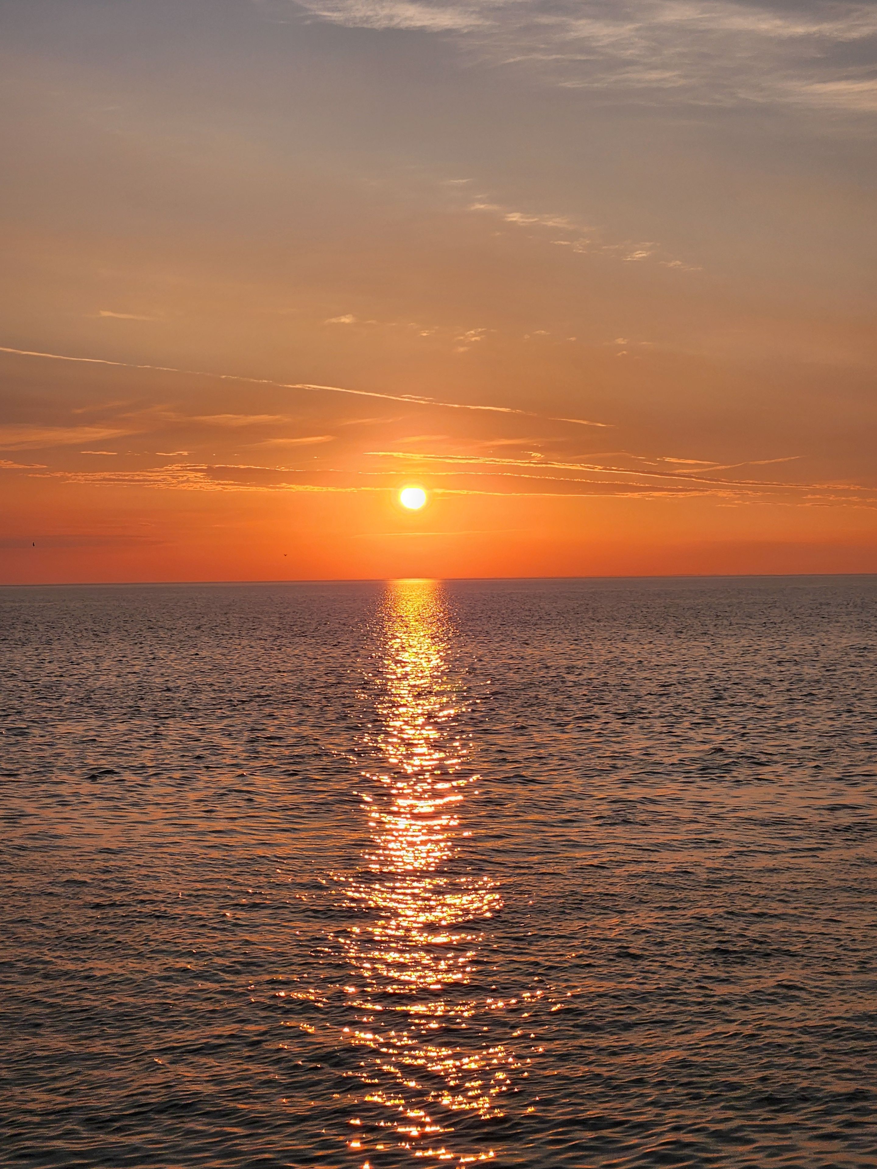 Ein Sonnenuntergang über einem ruhigen Meer mit sichtbarer Sonnenreflexion auf der Wasseroberfläche.