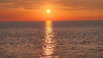 Pôr do sol sobre um mar calmo, com reflexo do sol na água.