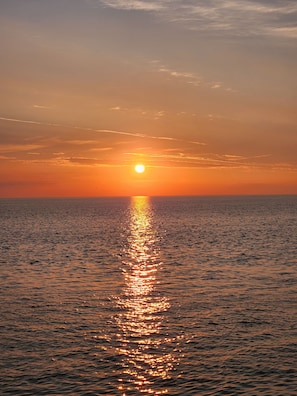 Ein Sonnenuntergang über einem ruhigen Meer mit sichtbarer Sonnenreflexion auf der Wasseroberfläche.