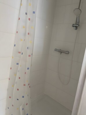 Ein Duschbereich mit weiß gefliester Wand, einer Duschbrause und einem Vorhang mit einem Muster aus Linien und Rechtecken.