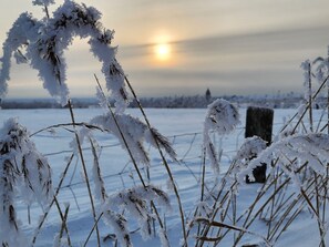 Een besneeerd landschap met een hek en een paal op de voorgrond, en een ondergaande zon in de verte.