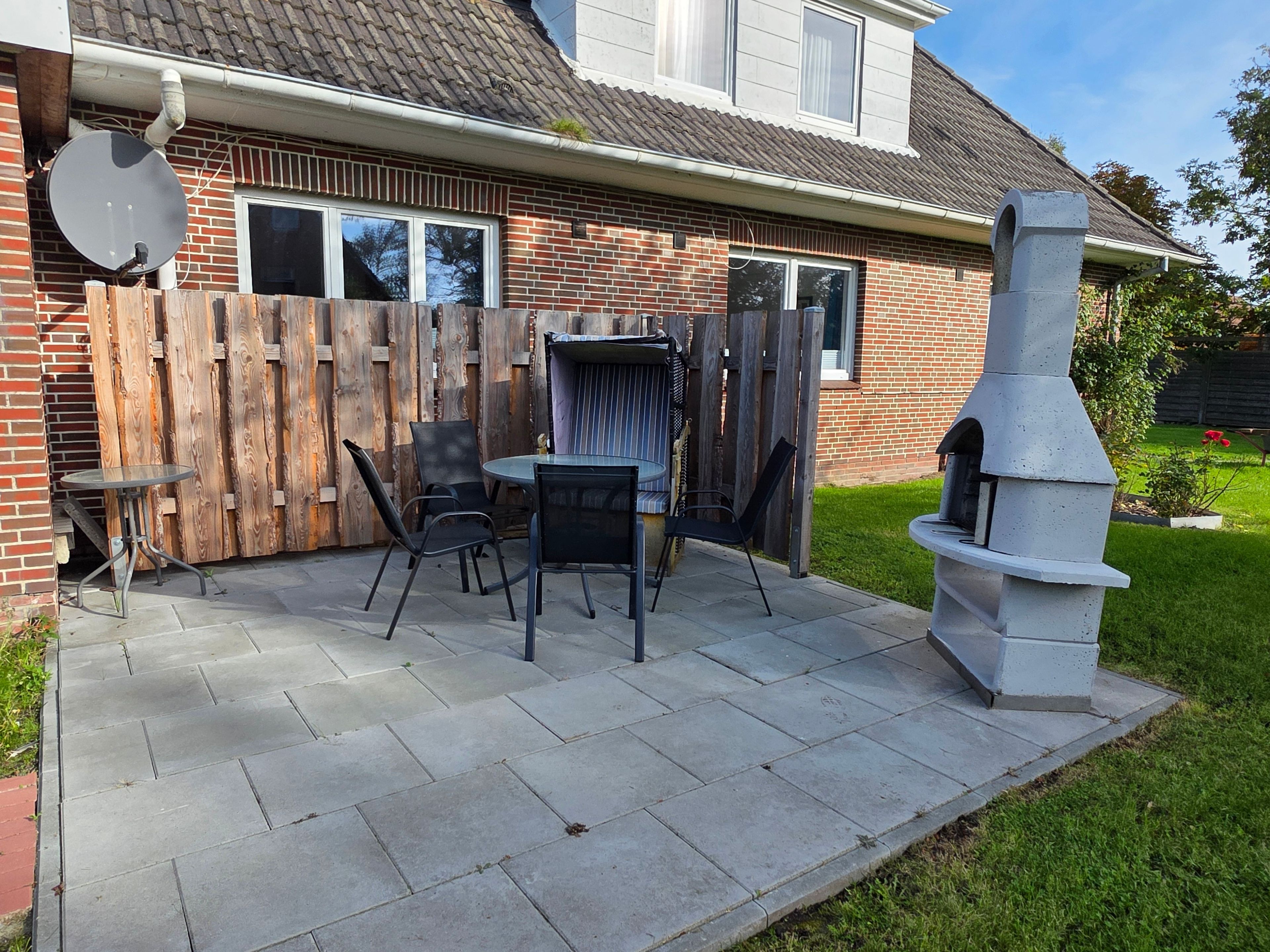 Un patio con una parrilla, zona de estar, una casa de ladrillo y una valla de madera.
