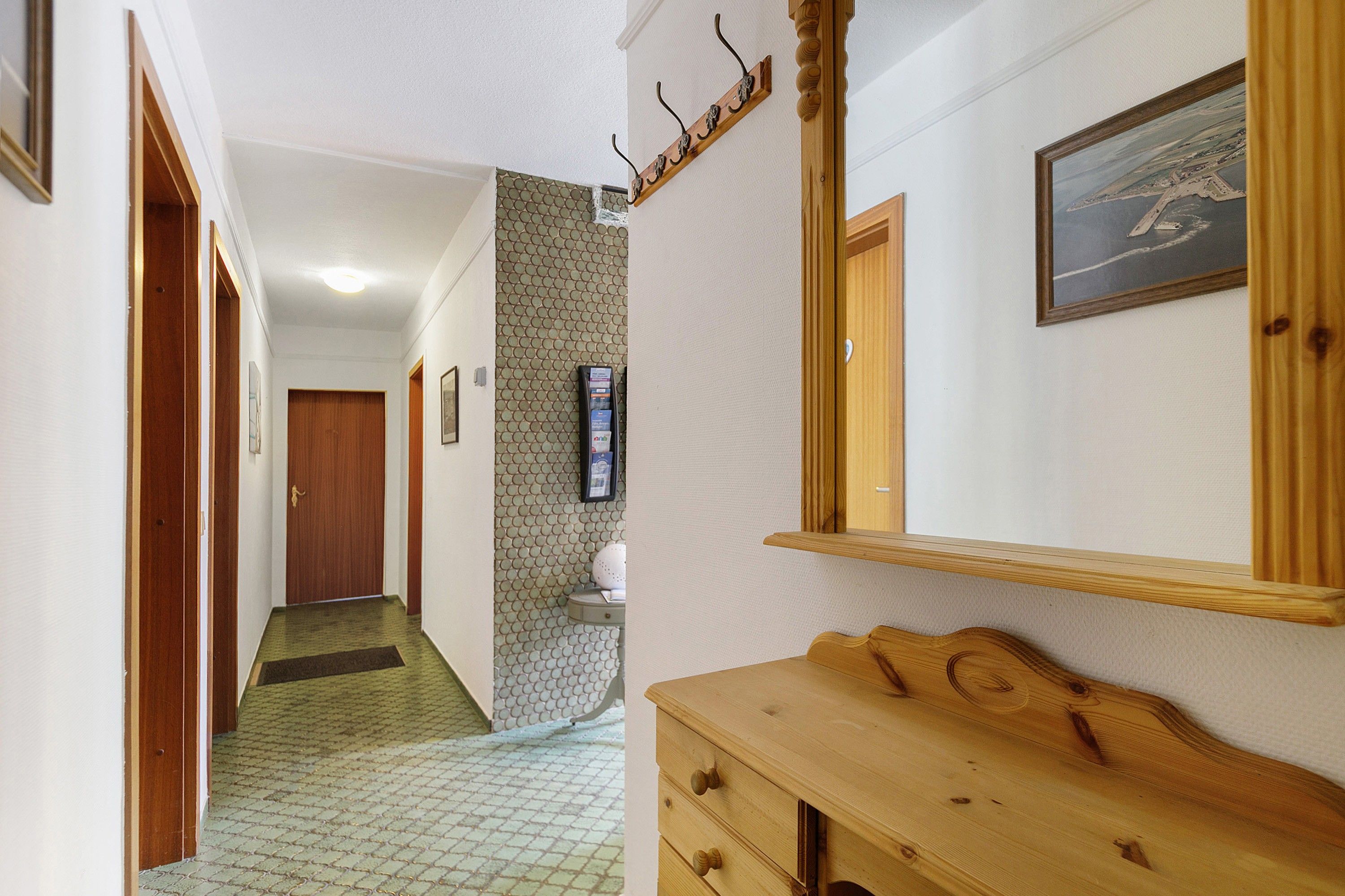 A hallway with a wooden bench, a door, a mirror, and a framed picture on the wall.