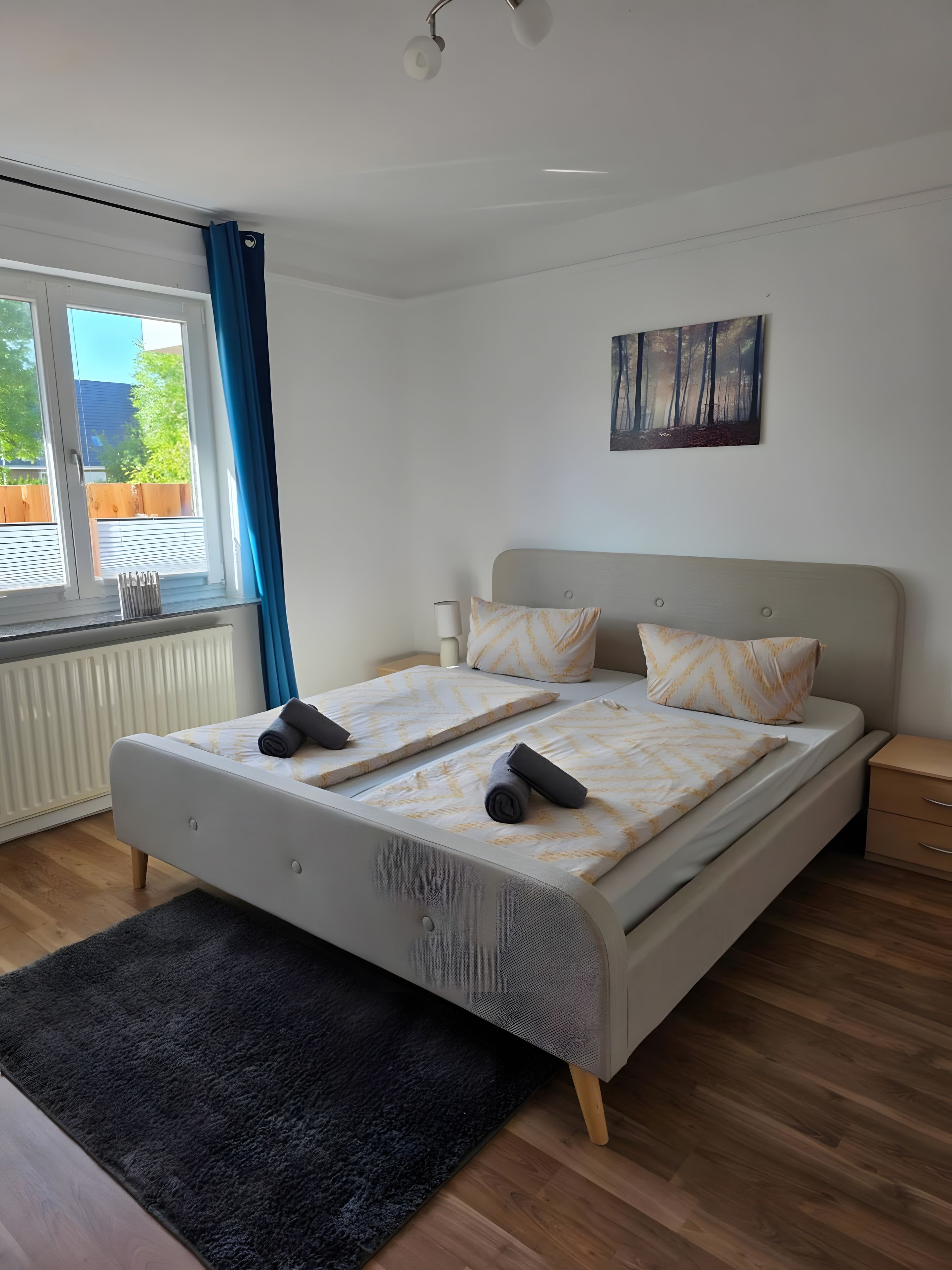 Quarto moderno com uma cama grande, janela com cortinas, radiador e um quadro na parede.