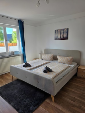 Quarto moderno com uma cama grande, janela com cortinas, radiador e um quadro na parede.
