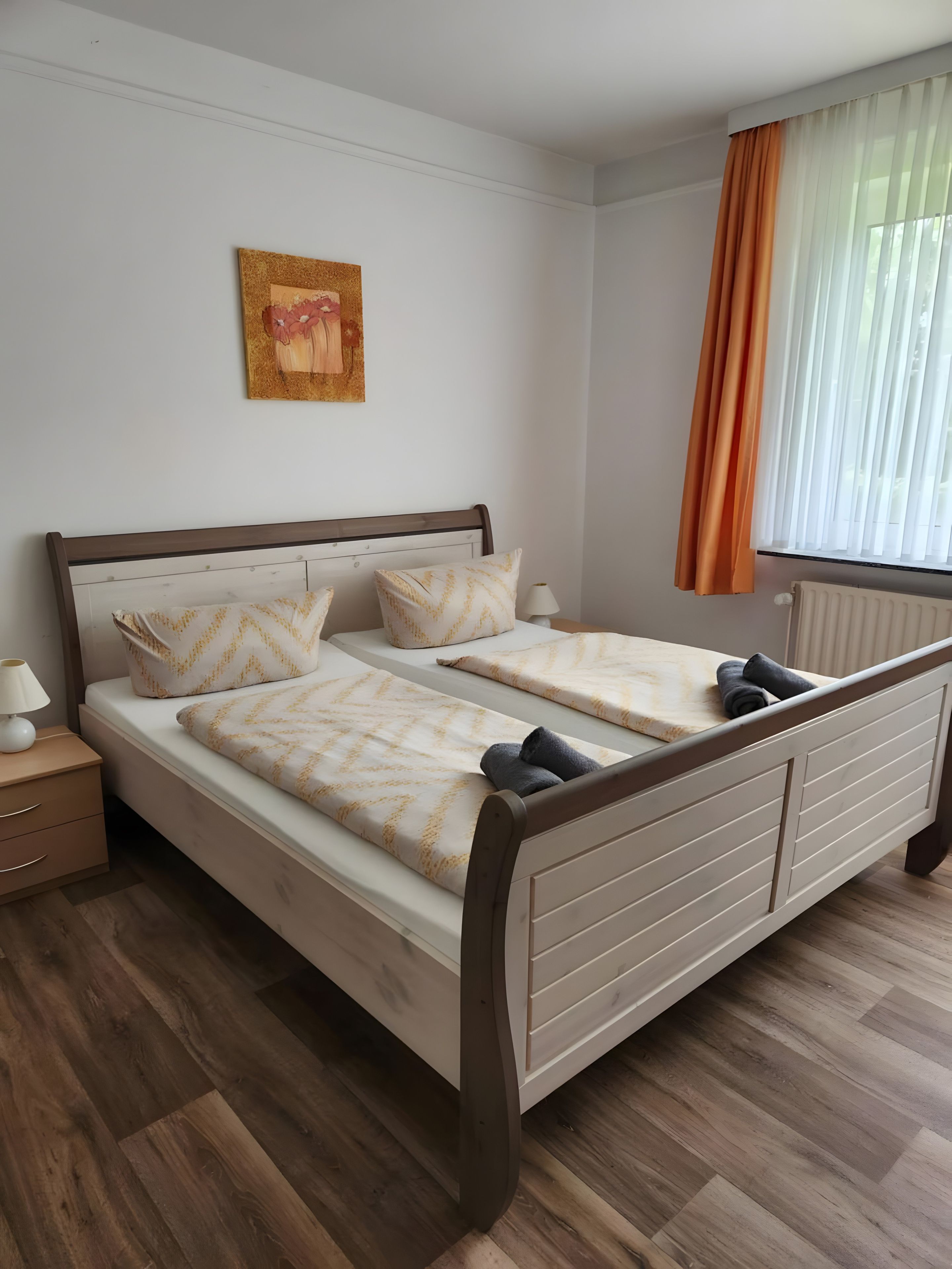 Un lit double avec une tête de lit, deux tables de chevet avec des lampes, un tableau accroché au mur et une fenêtre avec des rideaux.