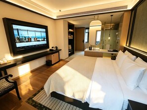 Habitación de hotel con cama, televisor montado en la pared, mesita de noche, espejo y baño con ducha y lavabo.