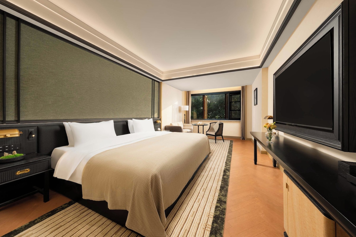 A hotel room with a large bed, a flat-screen TV, a desk, and a window.