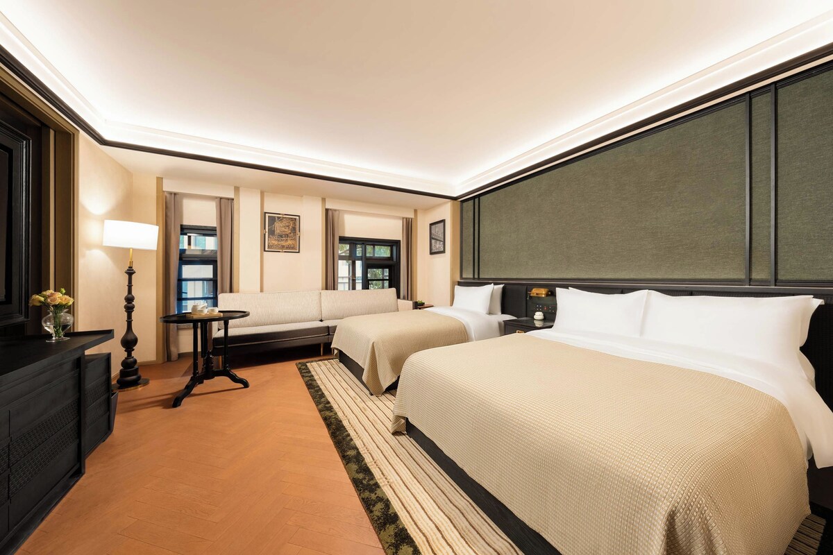 A hotel room with two beds, a sofa, a desk, and a window.