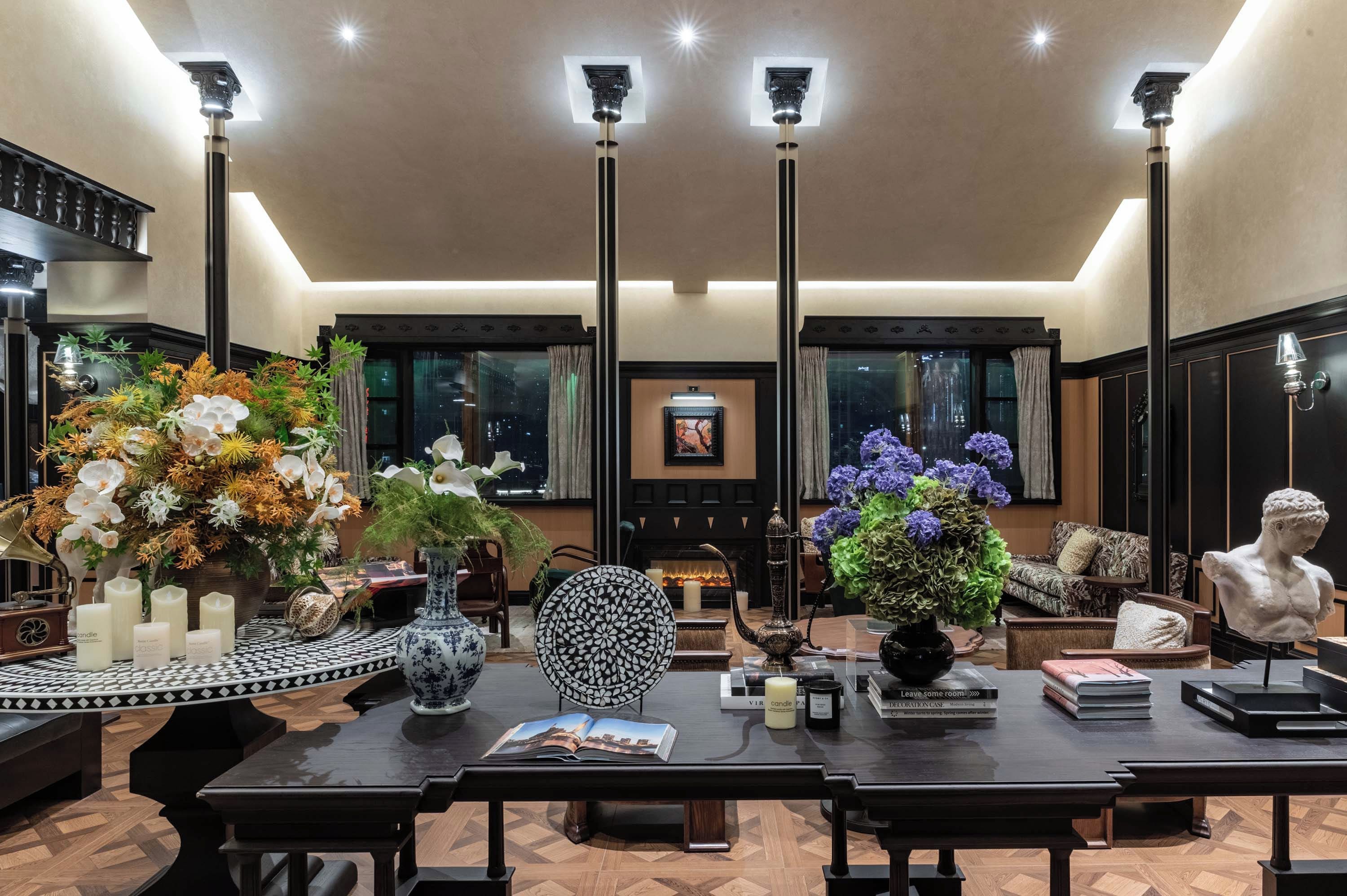 A spacious room with a large dining table, multiple vases with flowers, a fireplace, and a statue.