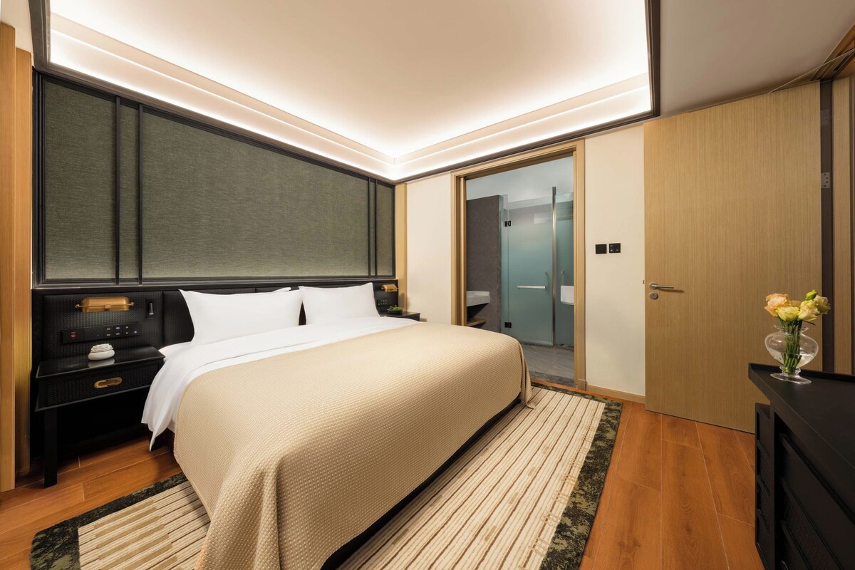 A modern bedroom with a large bed, bedside tables, a nightstand, a mirror, and a wardrobe.