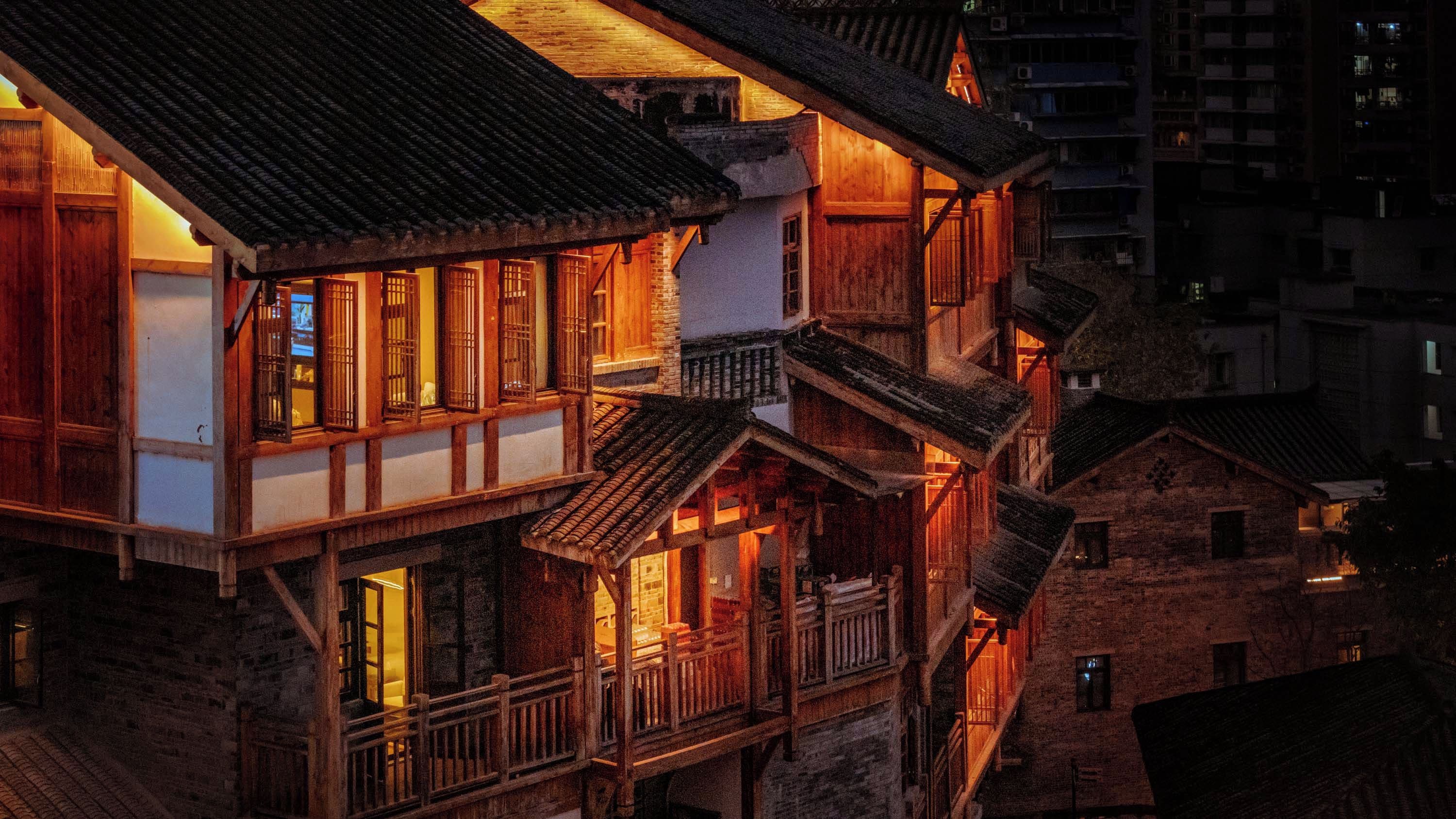 A traditional building with multiple levels and balconies, featuring wooden railings and a warm interior glow.