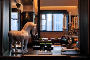 Una estatua de un caballo, un candelabro y libros sobre una mesa en una habitación con vistas a edificios a través de una ventana.