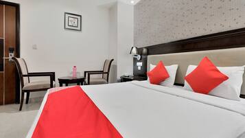 Quarto de hotel com cama, duas cadeiras, mesinha, criado-mudo e luminária na parede.