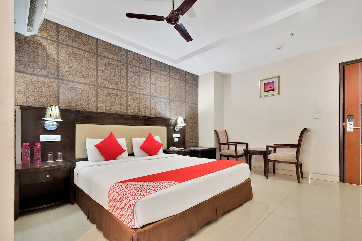 A hotel room with a large bed, a ceiling fan, a desk with a chair, and a small table.