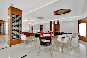 Una zona de menjador moderna amb una combinació de taules rodones i quadrades, algunes amb cadires, i una paret decorativa amb motius circulars.