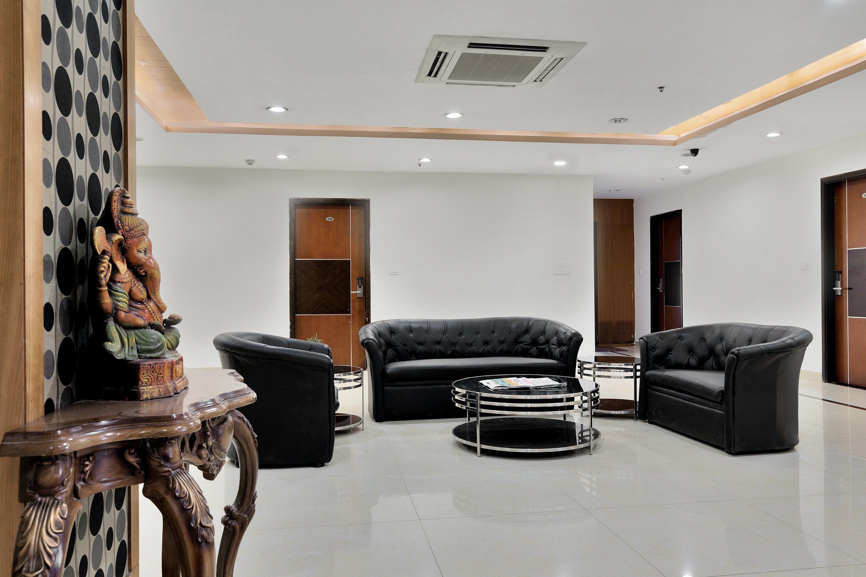 Um hall moderno com um sofá de couro preto, uma mesa de centro redonda de vidro e uma escultura decorativa de madeira.