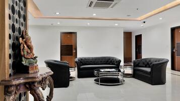 Um hall moderno com um sofá de couro preto, uma mesa de centro redonda de vidro e uma escultura decorativa de madeira.