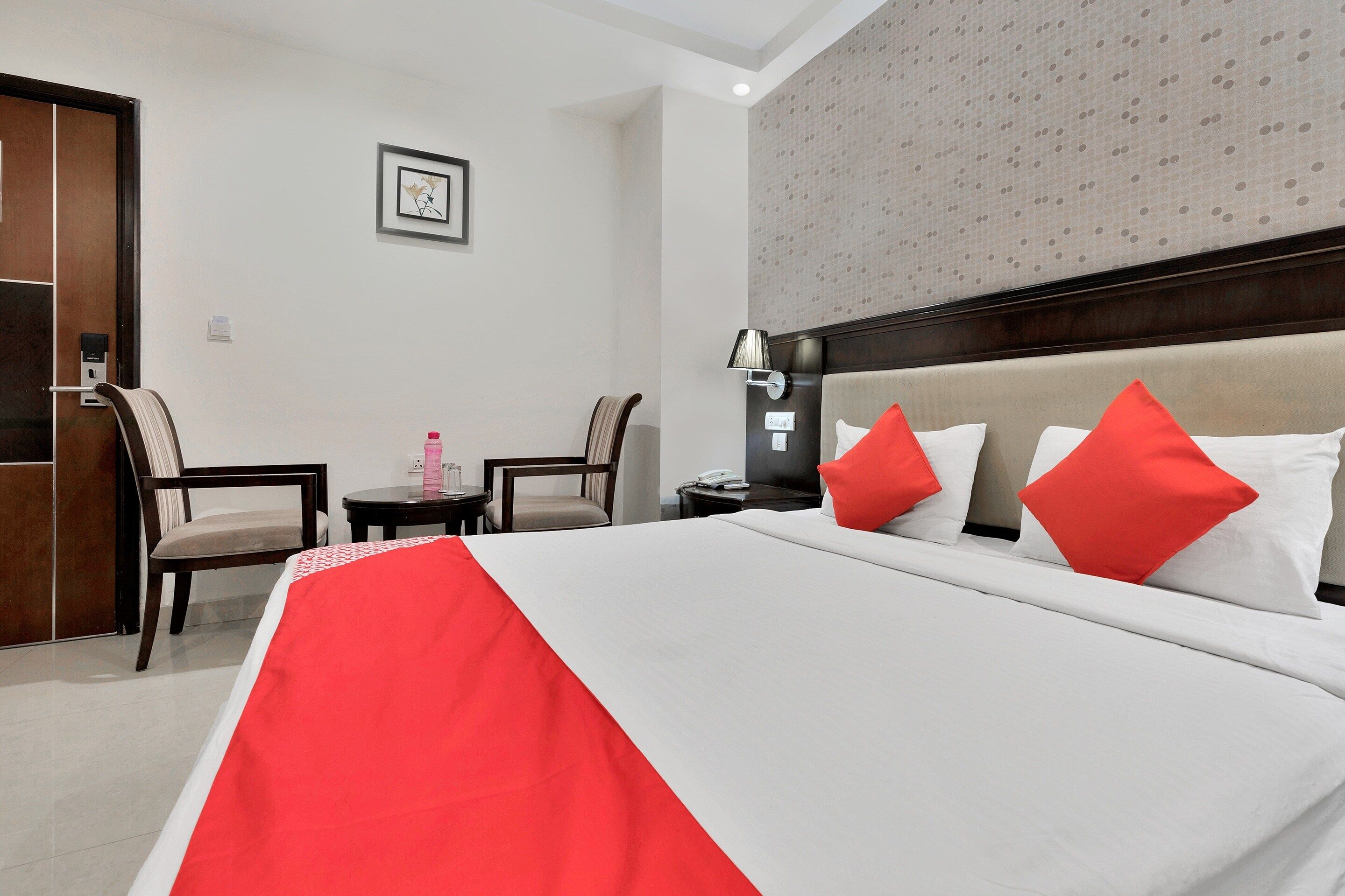 Habitación de hotel con una cama, dos sillones, una mesita de noche, una lámpara y un cuadro colgado en la pared.