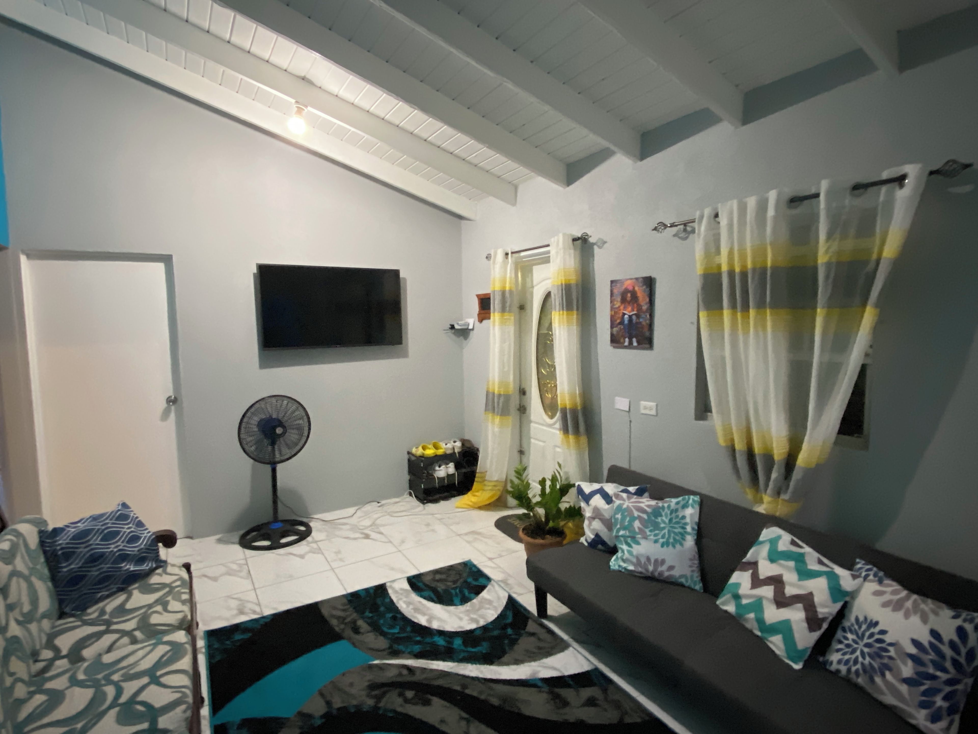 A living room with a sofa, a TV, a fan, and a door with curtains.