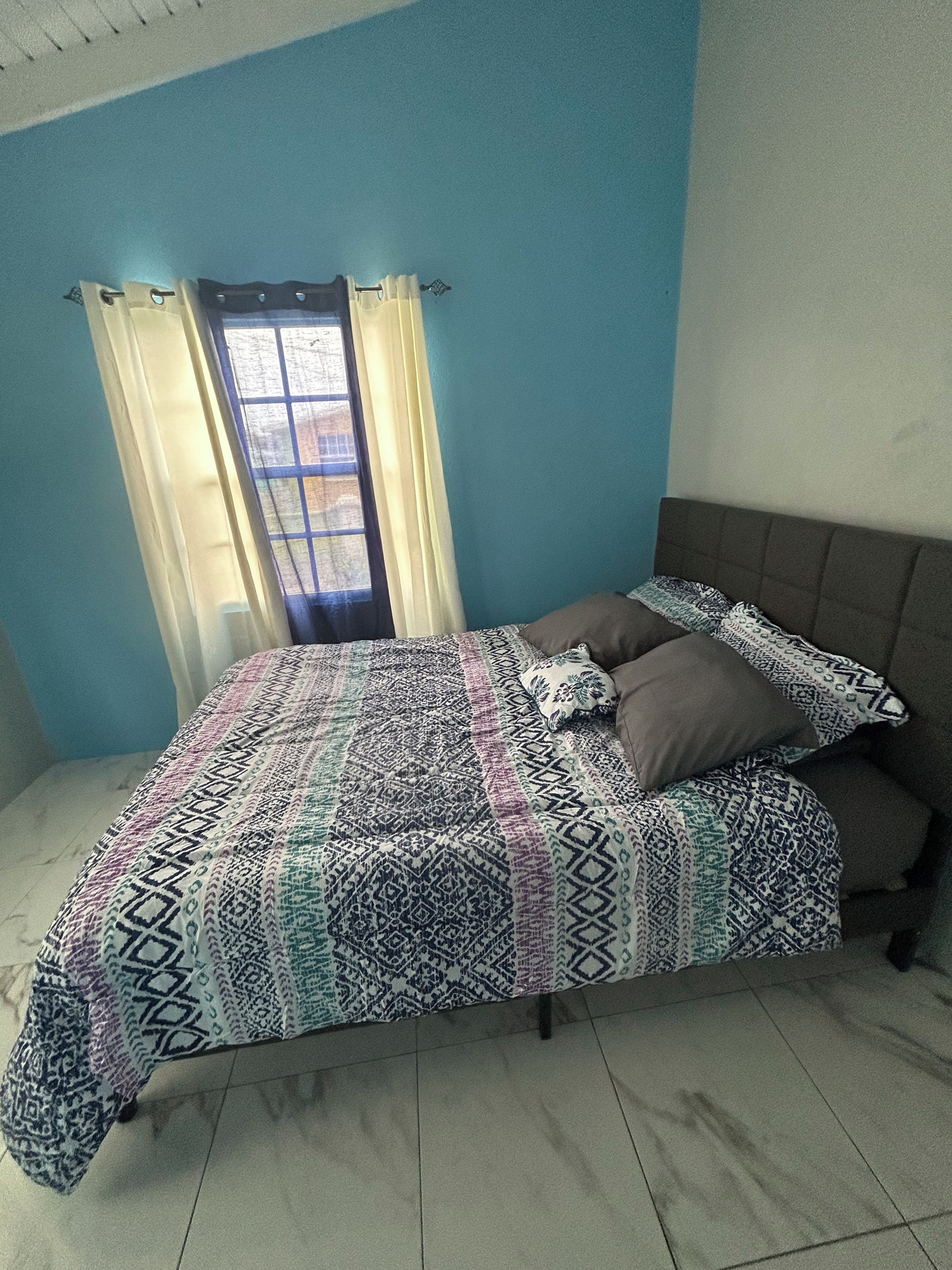 A bedroom with a bed, curtains, and a view through a window.