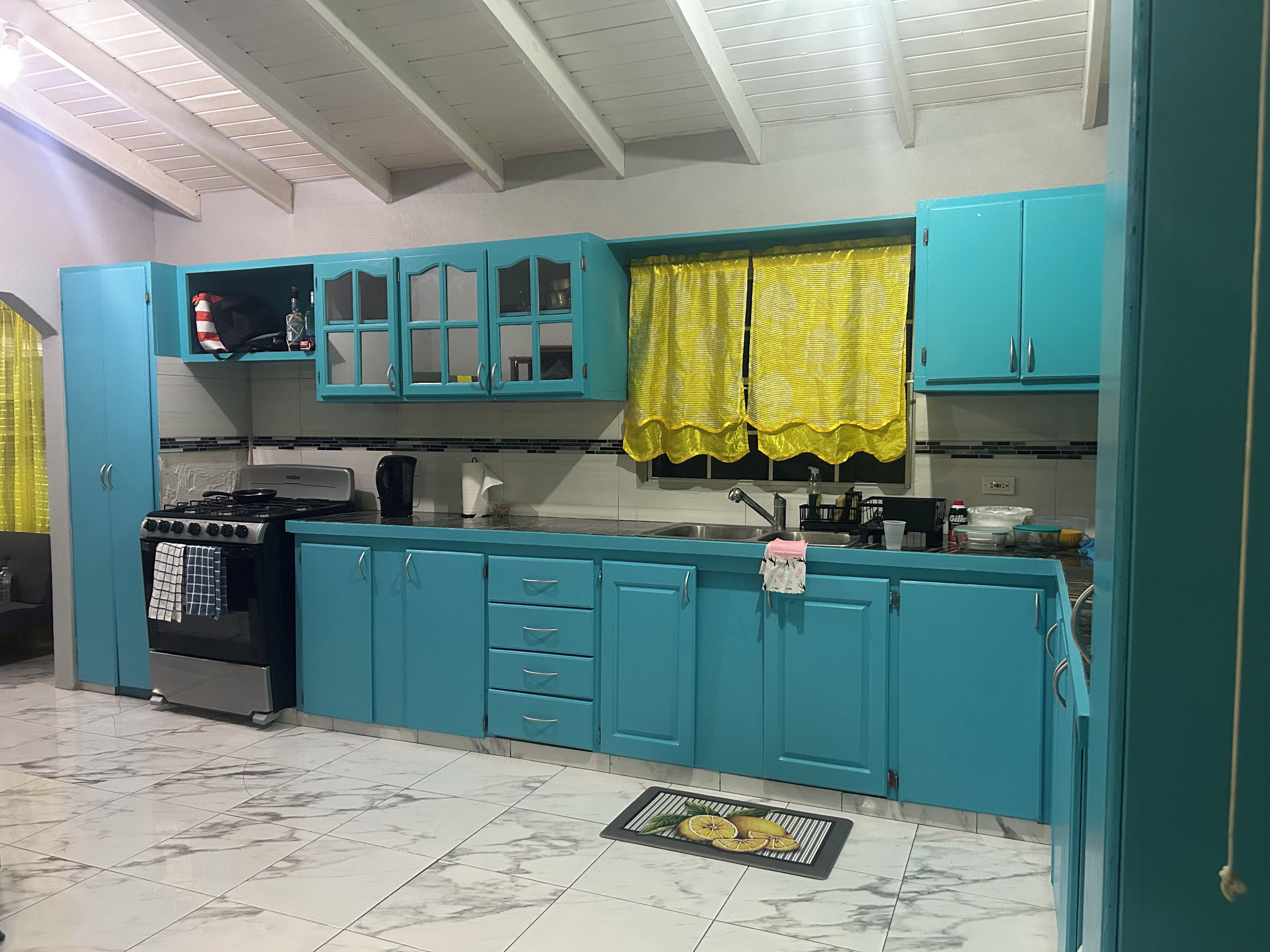 Una cucina con pensili color acquamarina, un fornello a gas e una tenda alla finestra color giallo.