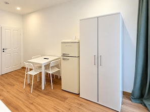 A room with a white table and chairs, a white refrigerator, and a wardrobe. - Unpack and Stay Vienna 1BR Westbahnhof (Vienna)