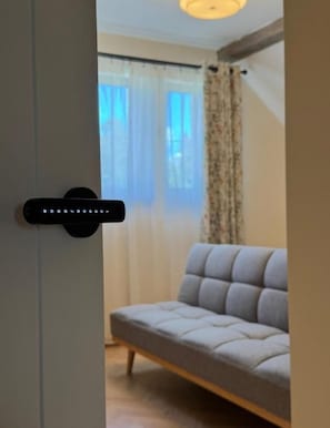Een kamer met een bank, een deur met slot en een raam met gordijnen.
