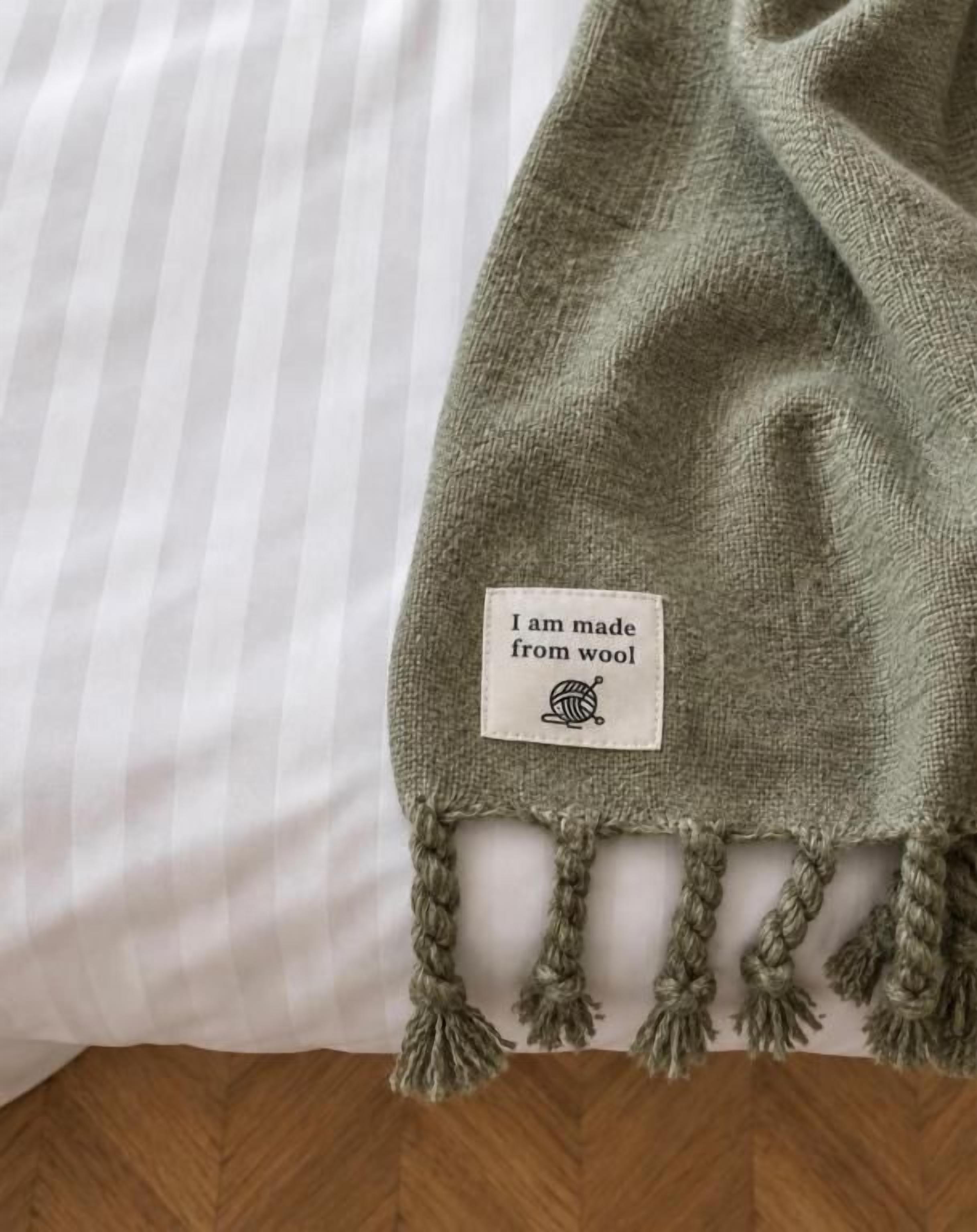 A green wool blanket with a tag on a bed.