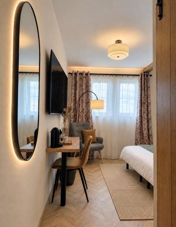 Una habitación de hotel con cama, escritorio, silla, televisor y un espejo grande.
