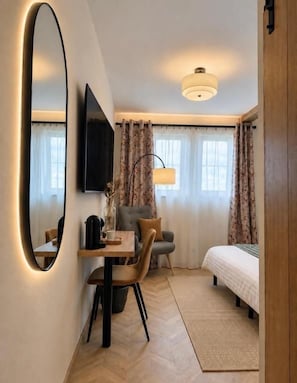 A hotel room with a bed, a desk with a chair, a television, and a large mirror.