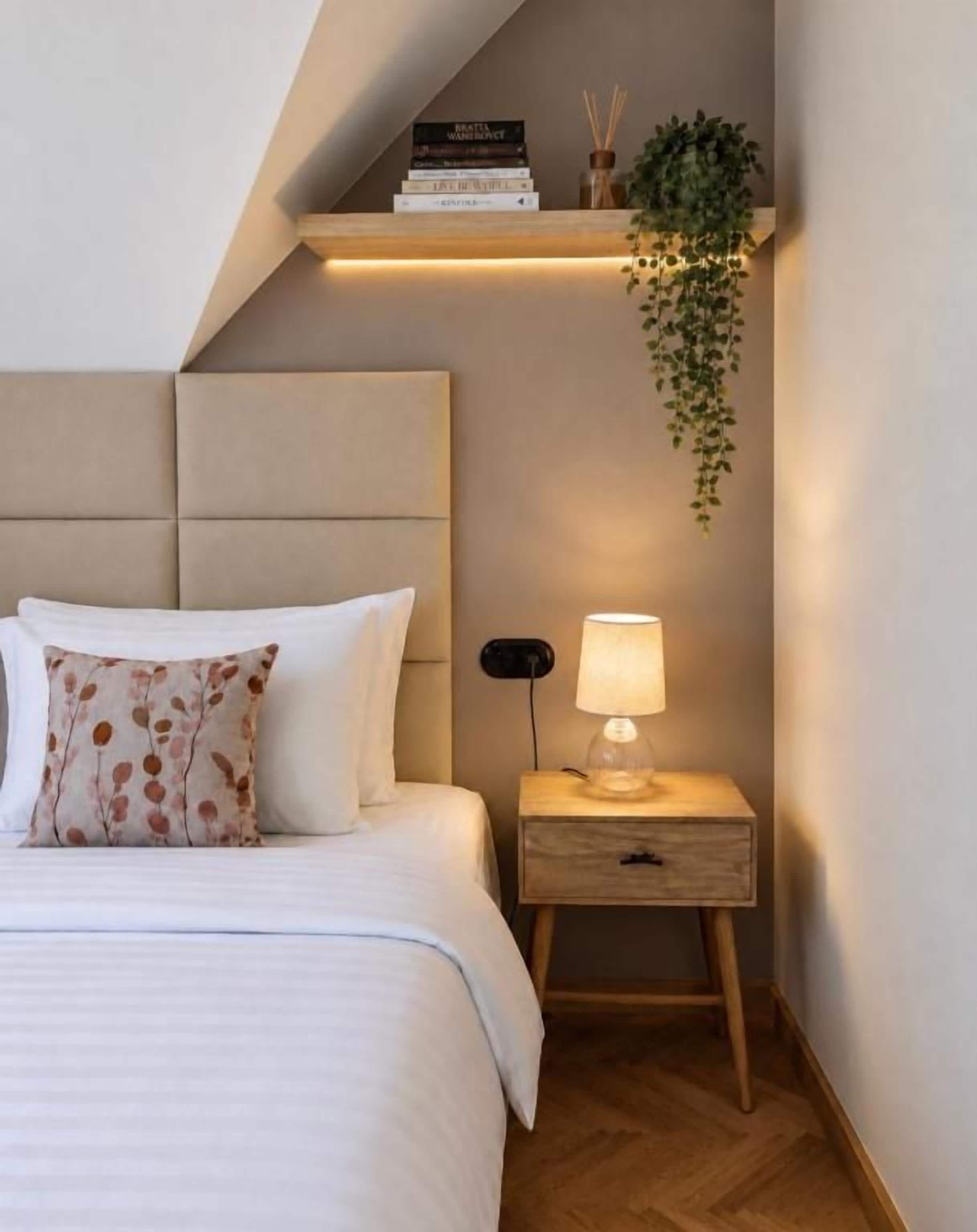Un dormitorio con una cama, mesita de noche, lámpara y una planta colgante.